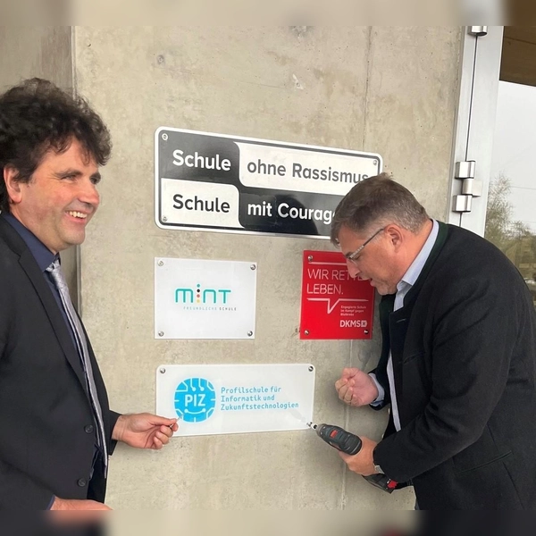 Landrat Stefan Löwl (rechts) und Christoph Strödecke, Schulleiter des Gymnasiums Markt Indersdorf, beim Anbringen der Auszeichnung „Profilschule für Informatik und Zukunftstechnologien“. (Foto: Landratsamt Dachau / Steffen Varga)